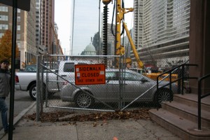 Cars are parked on the construction site behind a fence and this "Sidewalk Closed" sign on Arch Street between 19th and 20th, forcing pedestrians to cross mid-block. 