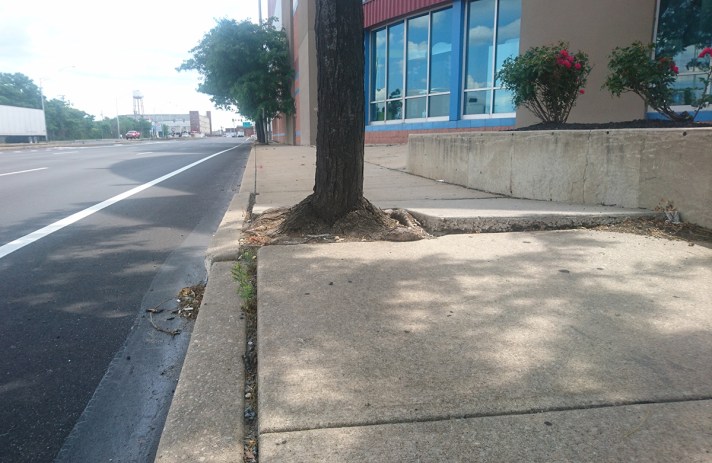 newly paved street with adjacent broken sidewalk,